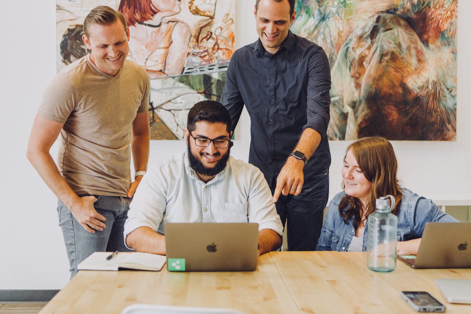 office team stands around looking at a colleague working on a laptop