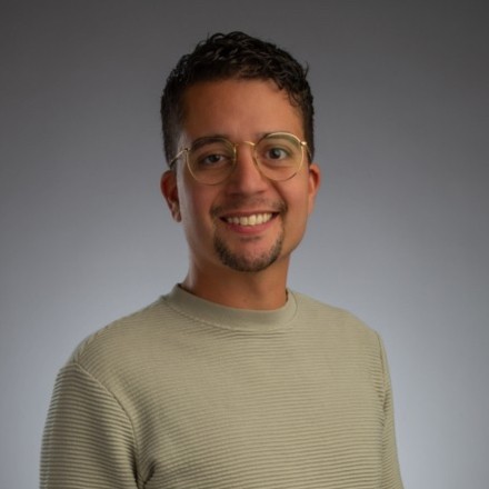 Richarc Reyes portrait style headshot, wearing a green sweater with glasses with dark hair